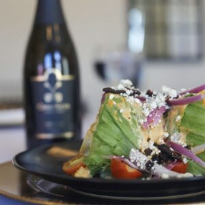 Plated salad with bottle of wine behind